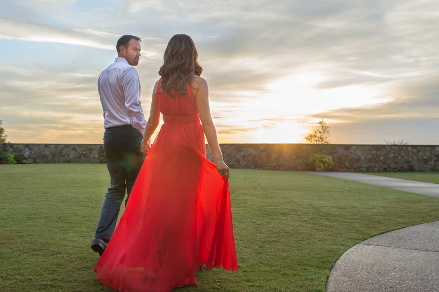 sun shining through woman's red dress while she walks with fiance