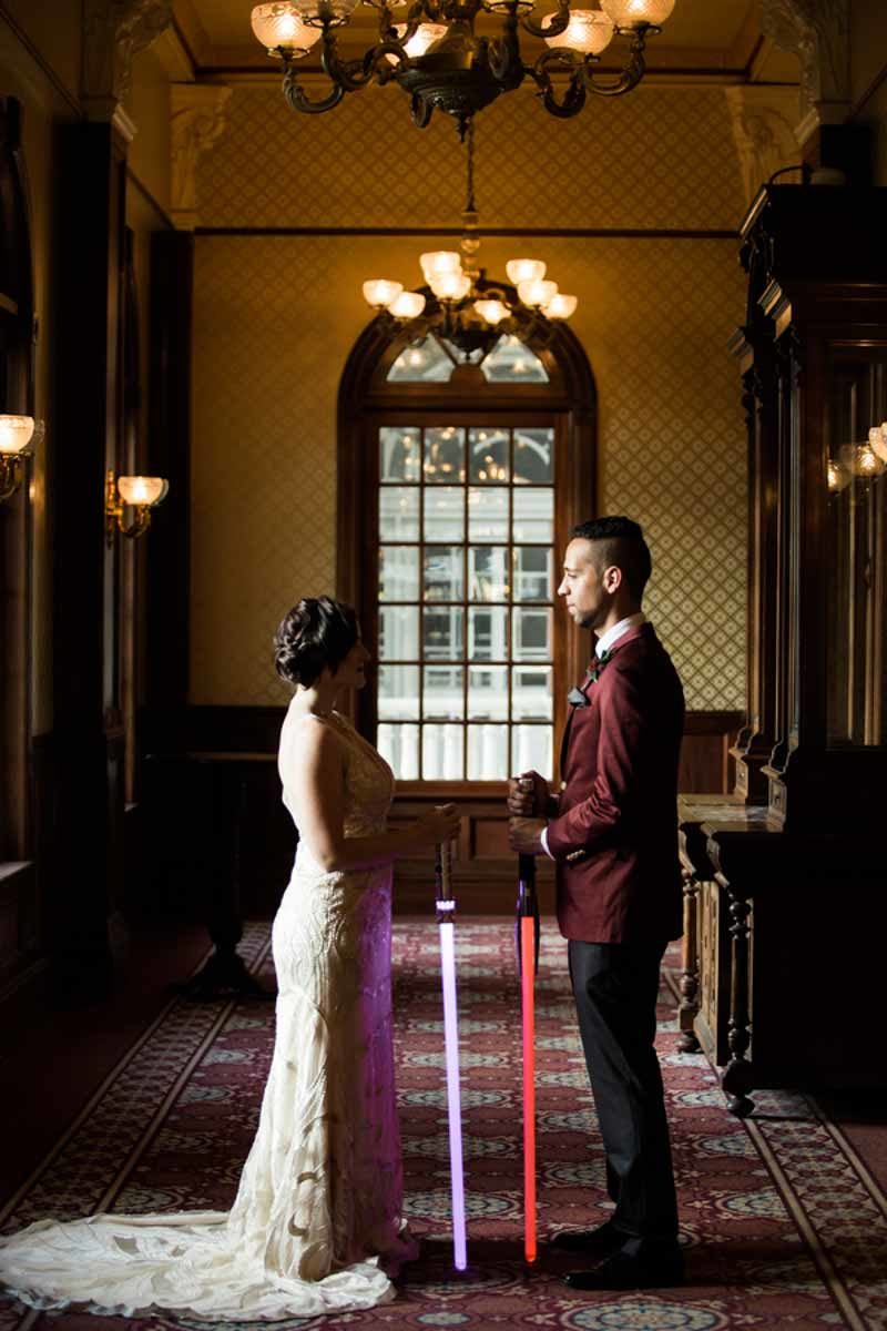 bride and groom holding lightsabers facing each other