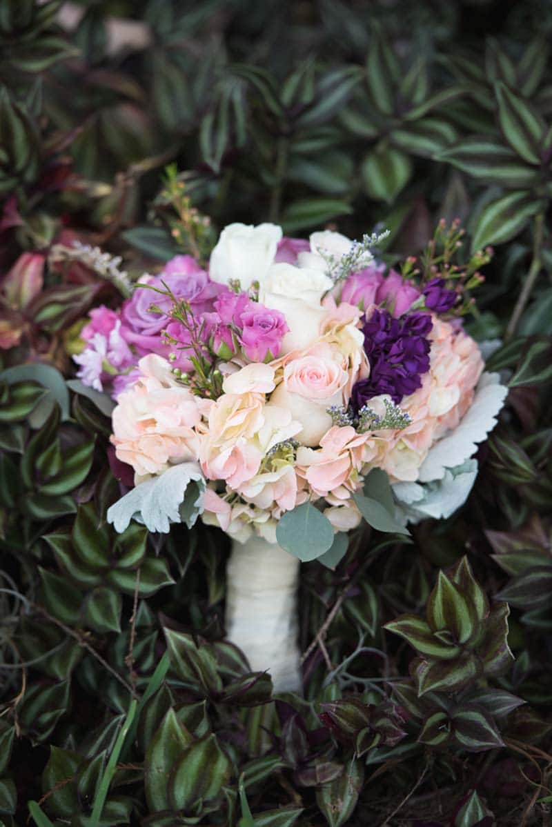 blush and purple wedding bouquet laying on bush