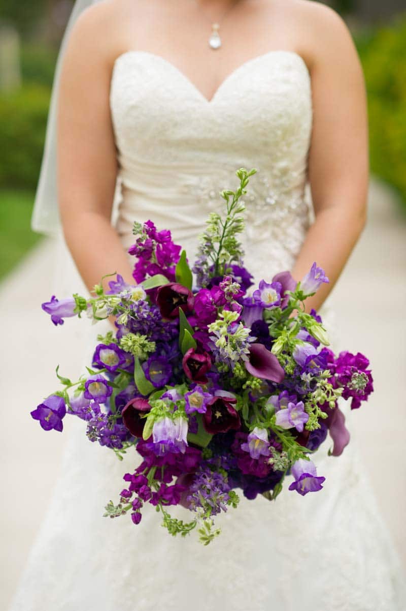bride holding green and dark purple bridal bouquet