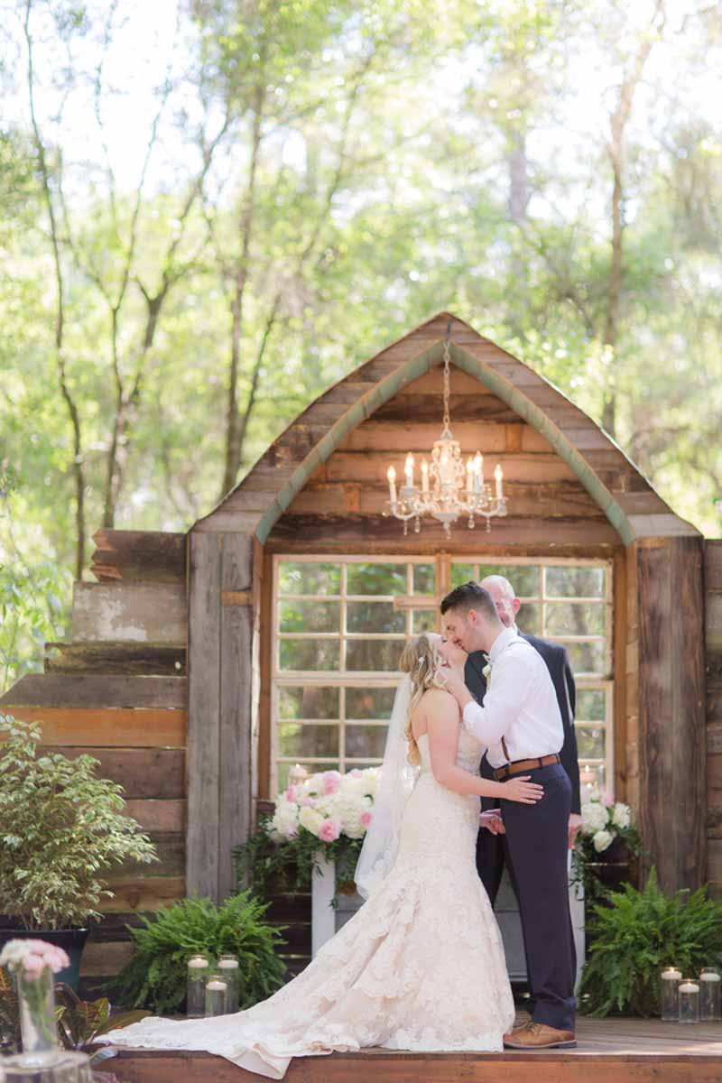 bride and groom's first kiss in front of rustic wedding ceremony space