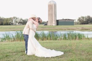 bride and groom kissing in front of pond and silo