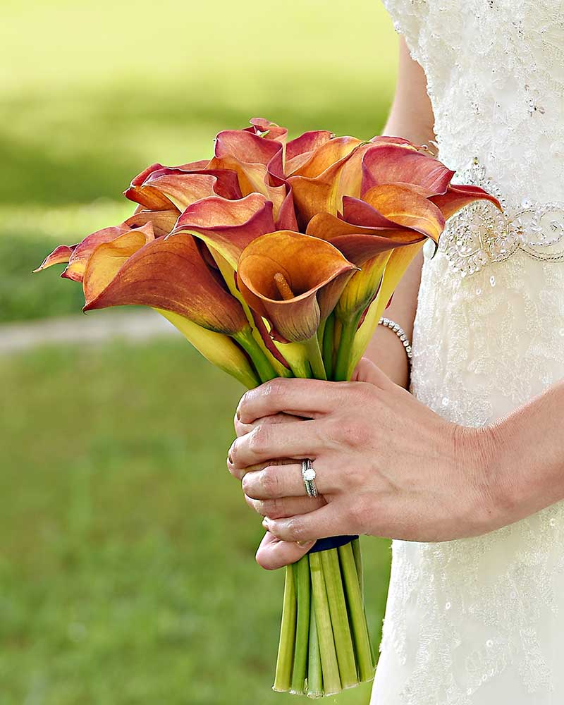 bride in grass holding red and orange calla lily bouquet