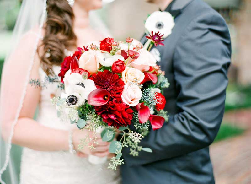 bride looking at groom while holding red and white bouquet