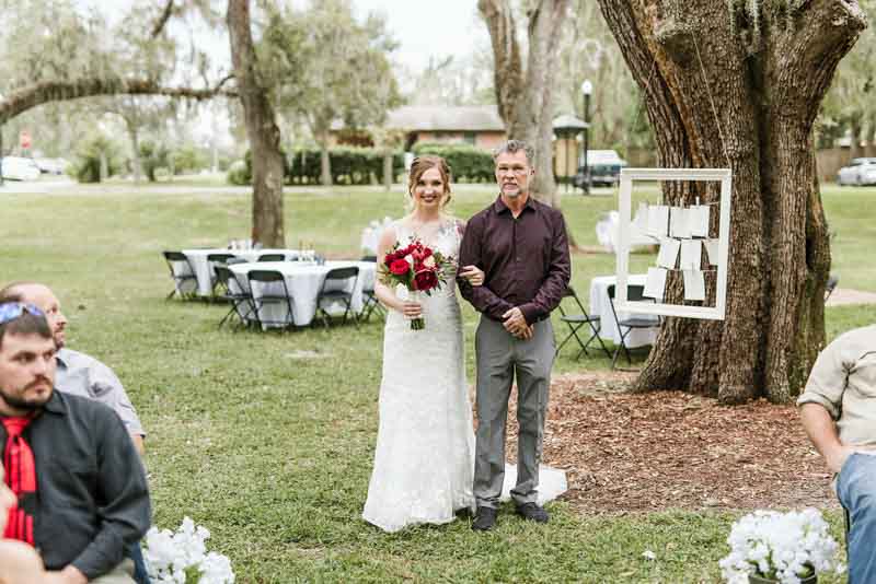 bride holding burgundy bouquet walking up aisle with father