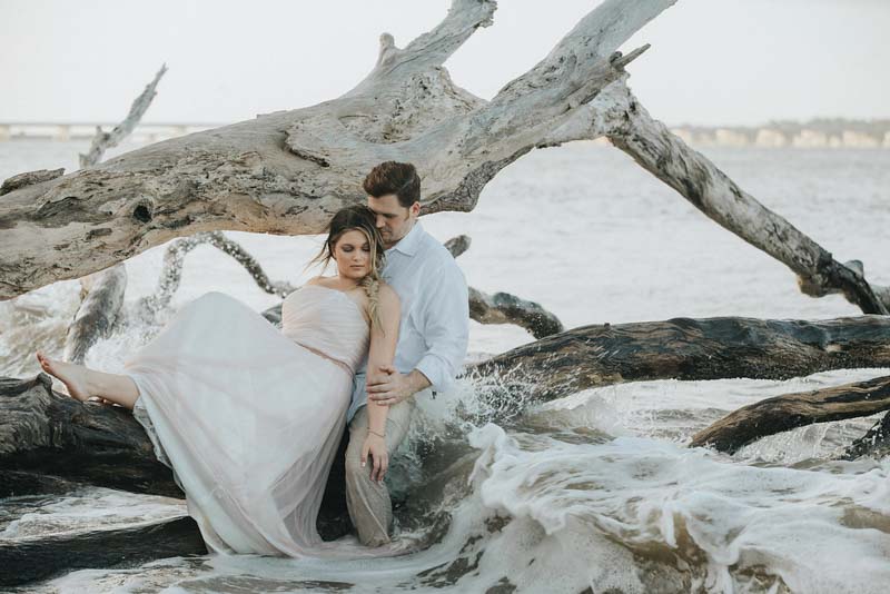 bride and groom sitting on driftwood
