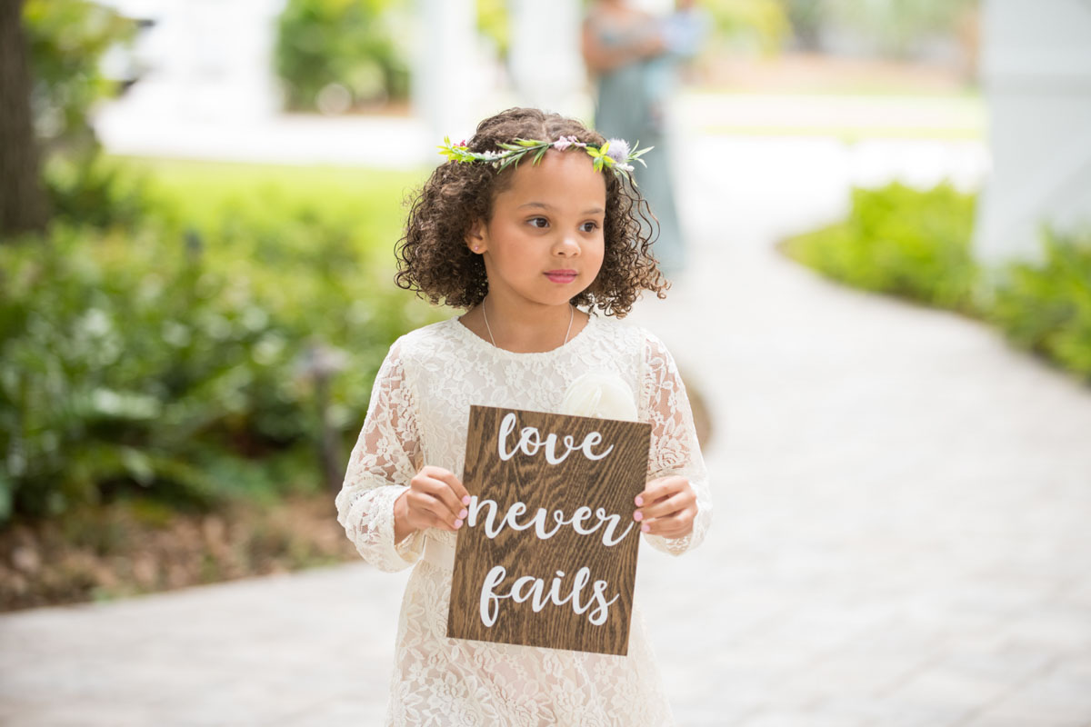 flower girl in flower crown holding a sign that says " love never fails"