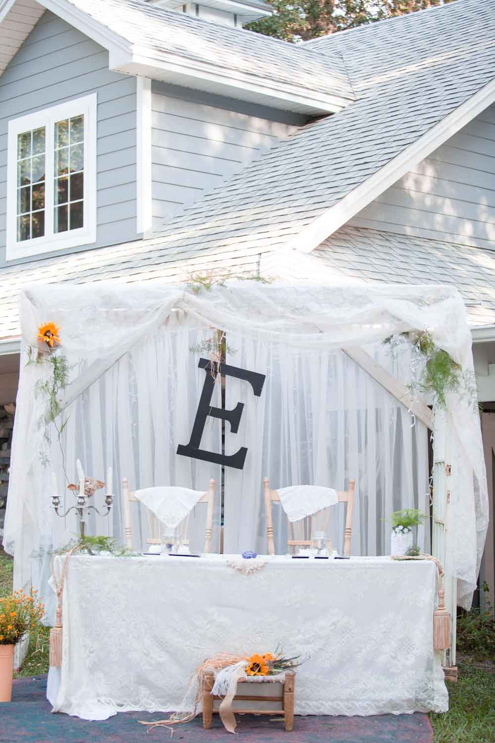wedding sweetheart table with white draping and large letter E on the backdrop