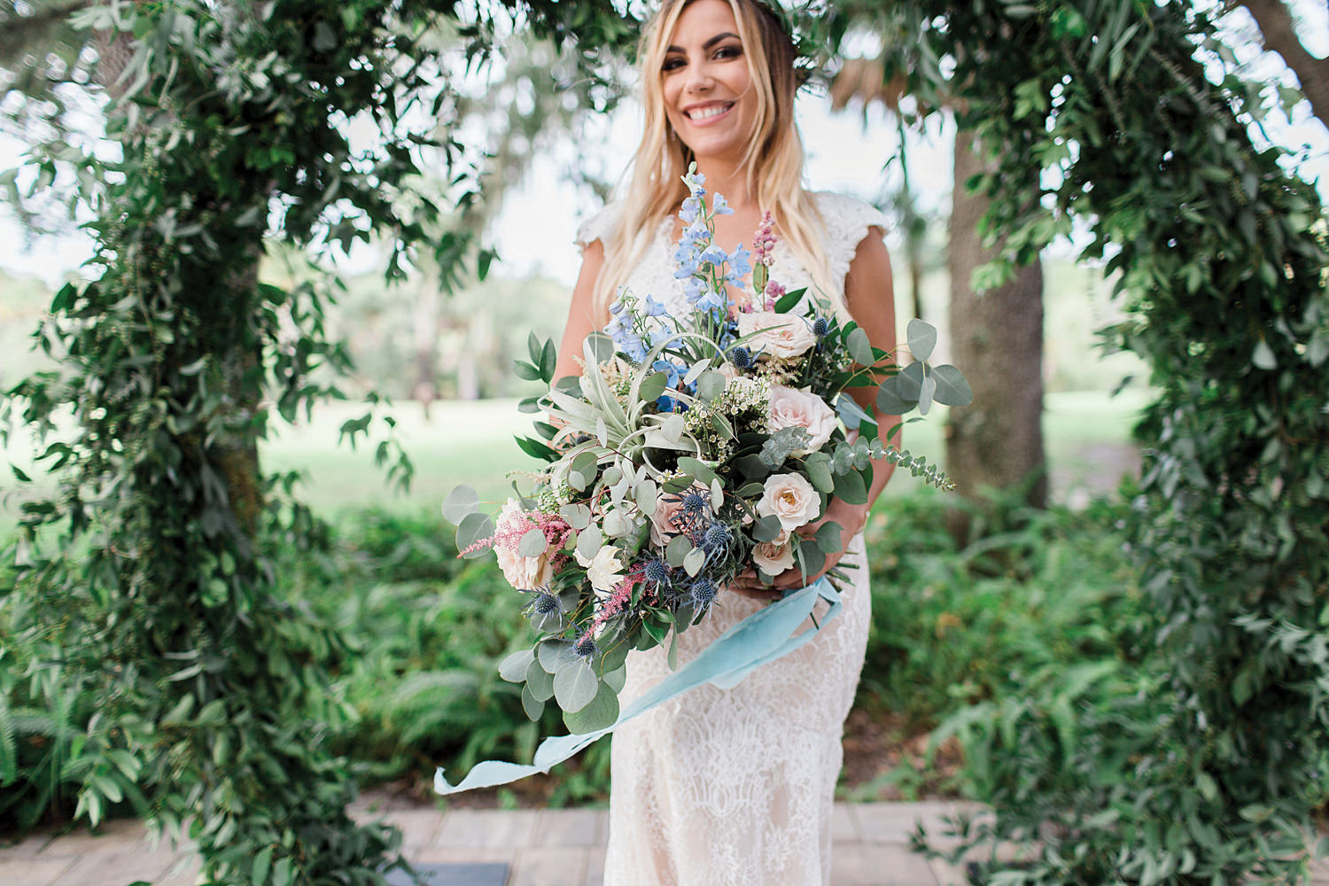 Bride holding her bouquet filled with blue, peach, blush, and greenery.