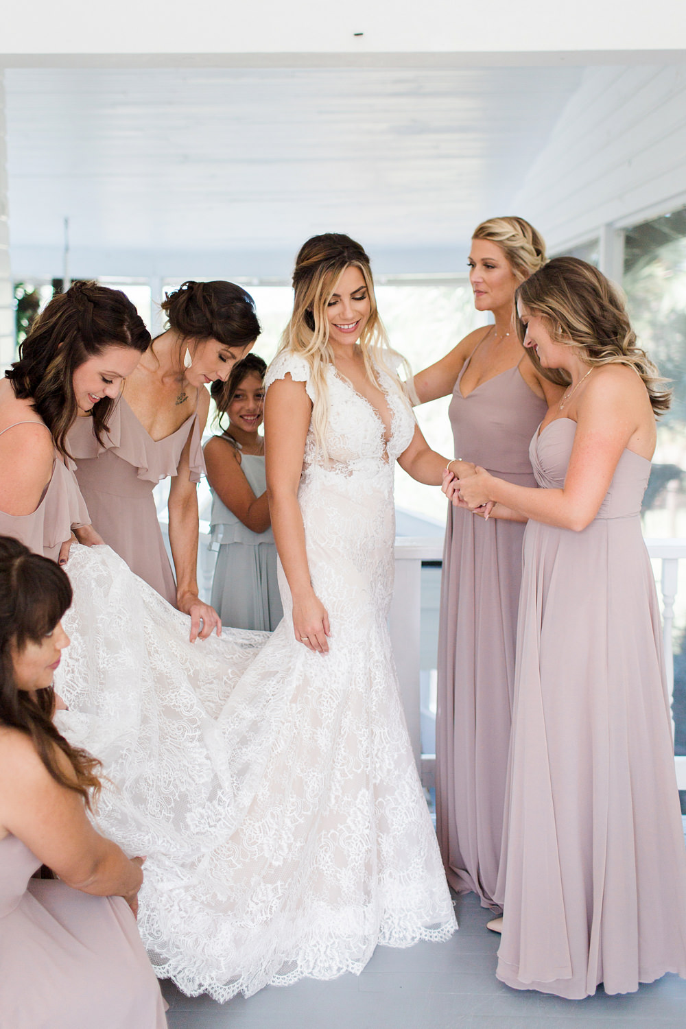 Bridesmaids, wearing mauve, helping the bride get in her dress.