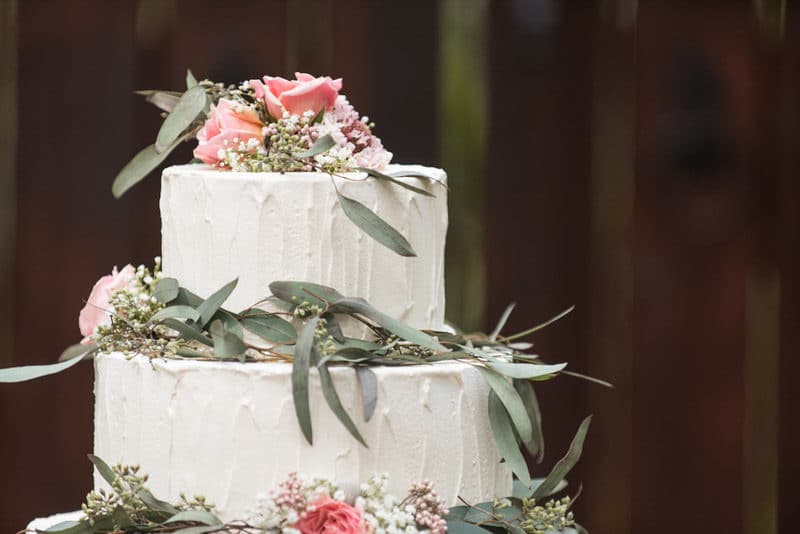 three tiered white buttercream wedding cake with greenery, pink roses, and baby's breathe
