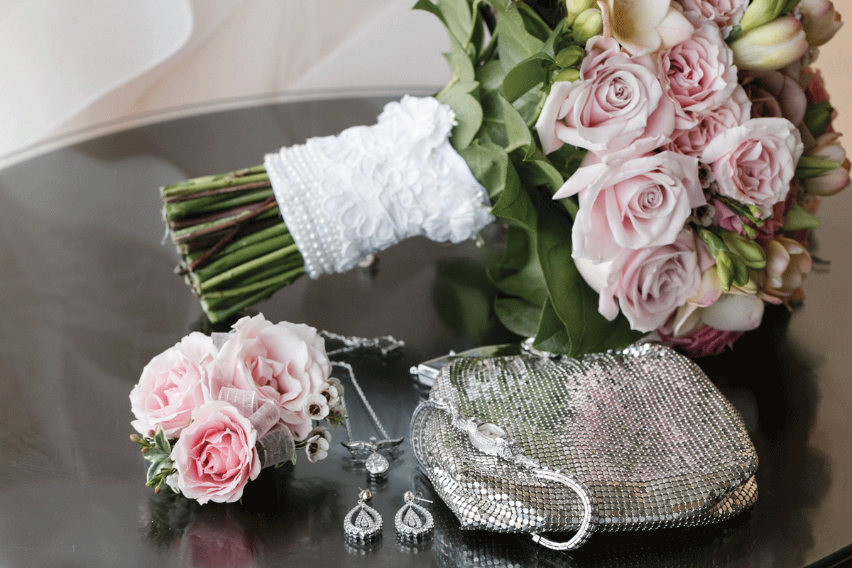 bridal bouquet with blush roses on table next to silver purse and family heirloom earrings