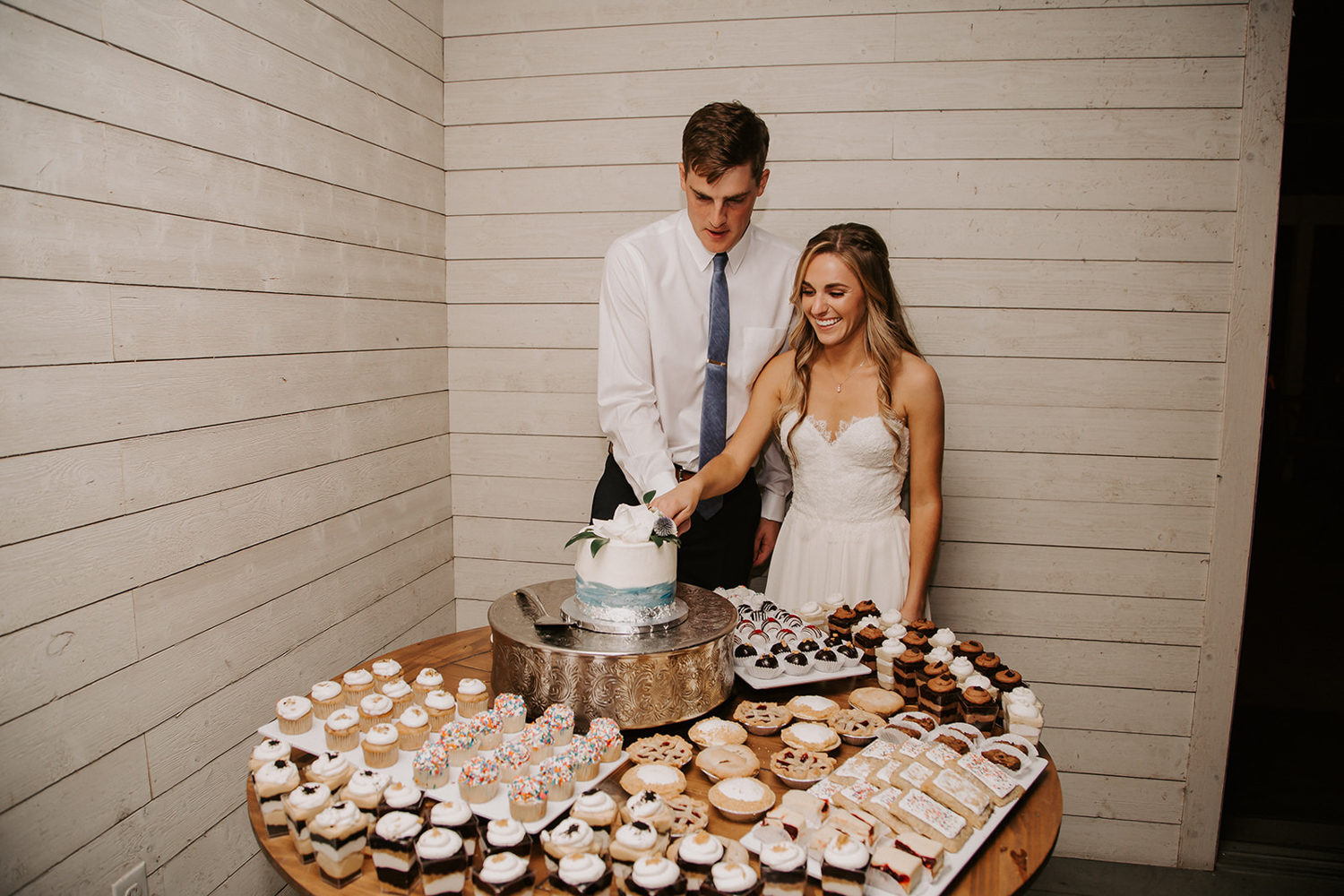 bride and groom cutting small cake on table with other desserts