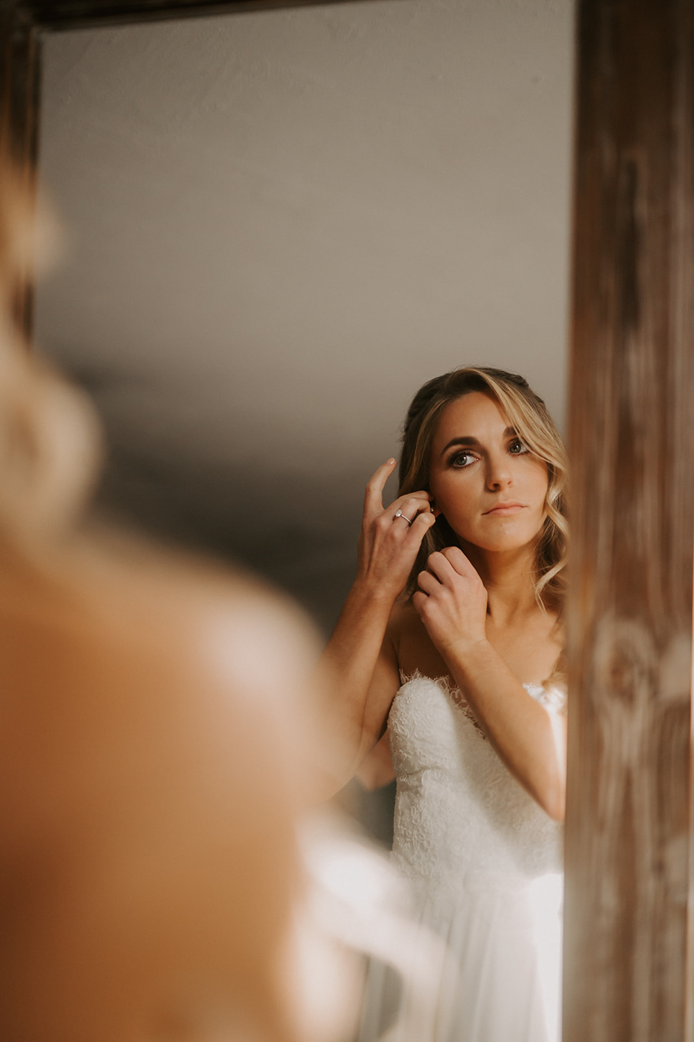 bride putting on earrings in mirror
