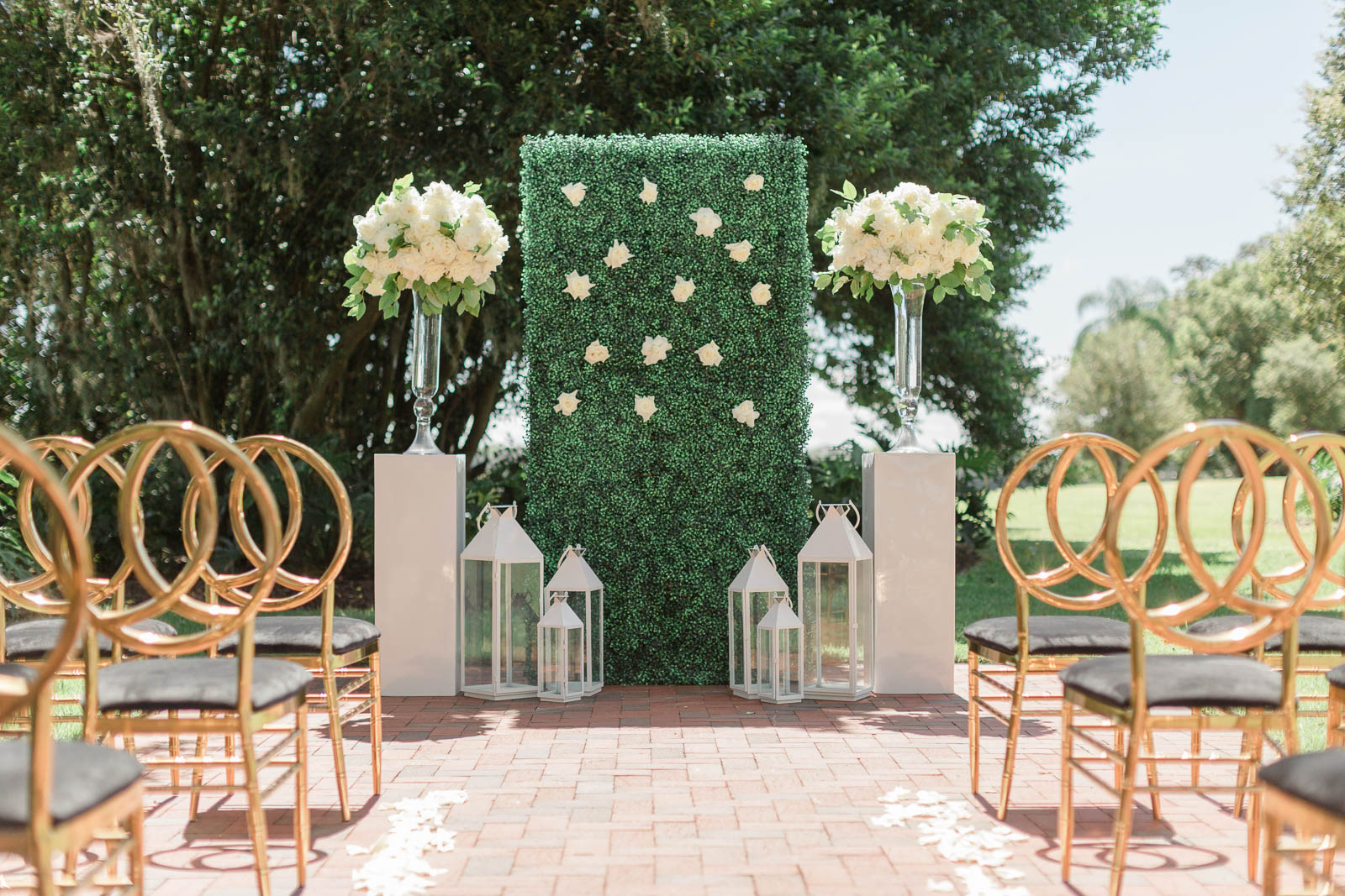 Hedge wall wedding ceremony backdrop with large white floral arrangements.