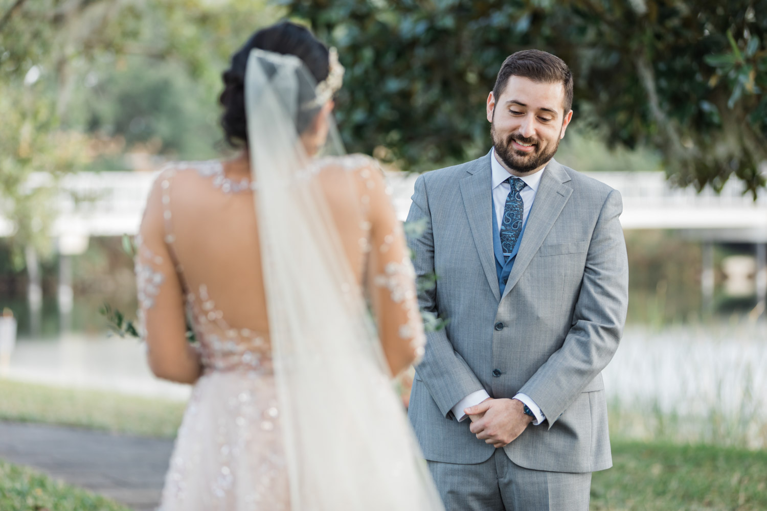 Groom in gray suit and blue tie smiling at bride during first look